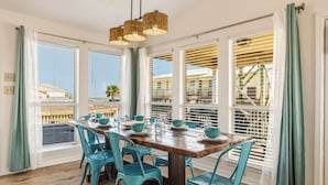 A dining area with a wooden table, teal chairs, and a hanging light fixture. - Mac's Crab Shack | Ocean Views | Great Location (Dauphin Island)