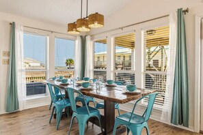 A dining area with a wooden table, teal chairs, and a hanging light fixture. - Mac's Crab Shack | Ocean Views | Great Location (Dauphin Island)