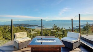 Una terraza con dos sillas de mimbre, una mesa de vidrio y vista a un lago y montañas.
