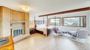 Un dormitorio con chimenea de ladrillo, una cama con dosel, una mesita de noche, una silla y ventanas amplias con vistas.