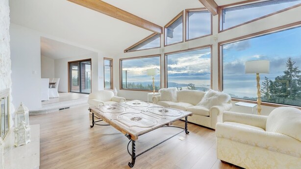 Amplia sala de estar con una gran mesa de madera, sofás blancos y vistas al exterior a través de amplios ventanales.