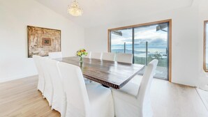 Un comedor moderno con una mesa de madera, sillas blancas, una araña y un ventanal con vistas.