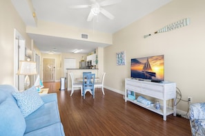 Ein Wohnzimmer mit einer Couch, einem Esstisch mit Stühlen, einer TV-Konsole mit Fernseher und einem Deckenventilator.
