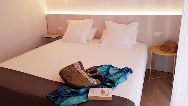 Una habitación de hotel con una cama, mesitas de noche, una lámpara y un sombrero en una silla.