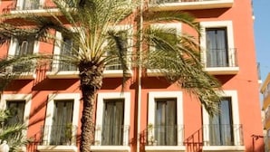 Un edificio de varios pisos con balcones, una palmera en primer plano y cielo despejado.