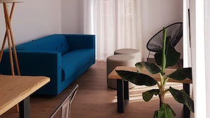 Una sala moderna con un sofá azul, un otoman redondo, una silla negra y una mesa de madera.