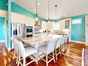 A modern kitchen with white cabinetry, a large island with chairs, stainless steel appliances, and pendant lighting. - | Azure Haven, Roof top deck, pool & spa (St. Augustine)