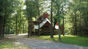 A wooden cabin with a deck and stairs, surrounded by trees.