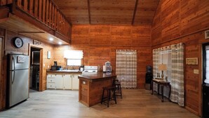 A wooden cabin interior with a kitchen, a dining area, and a bar.