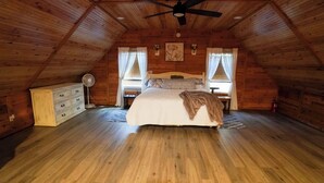 A cozy attic bedroom with a wooden ceiling, a bed, a dresser, and a fan.