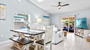 A spacious living area with a dining table, white furniture, a ceiling fan, and a TV. - Indialantic Oasis | 2BR, Outdoor Screened-in Patio & BBQ Grill! 🌴🌊 (Indialantic)