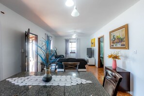 A modern living room with a sofa, TV, and a dining area with a table and chairs. - Casa com Churrasqueira e Rede a 210 m da Praia (Navegantes)