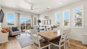 A spacious dining area with a wooden table and white chairs, large windows with blinds, and a ceiling fan. - The Retreat Resort Amenities New Listing (Washington)