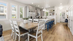 A modern kitchen with white cabinetry, a central island, and a dining area with white chairs. - The Retreat Resort Amenities New Listing (Washington)