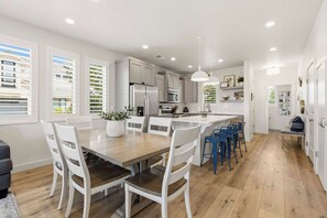 A modern kitchen with white cabinetry, a central island, and a dining area with white chairs.