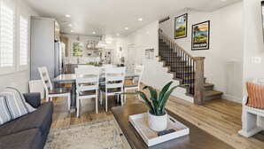 A modern kitchen with white cabinets, a dining area with a white table and chairs, a staircase with wooden steps, and a living room with a sofa and a coffee table. - The Retreat Resort Amenities New Listing (Washington)