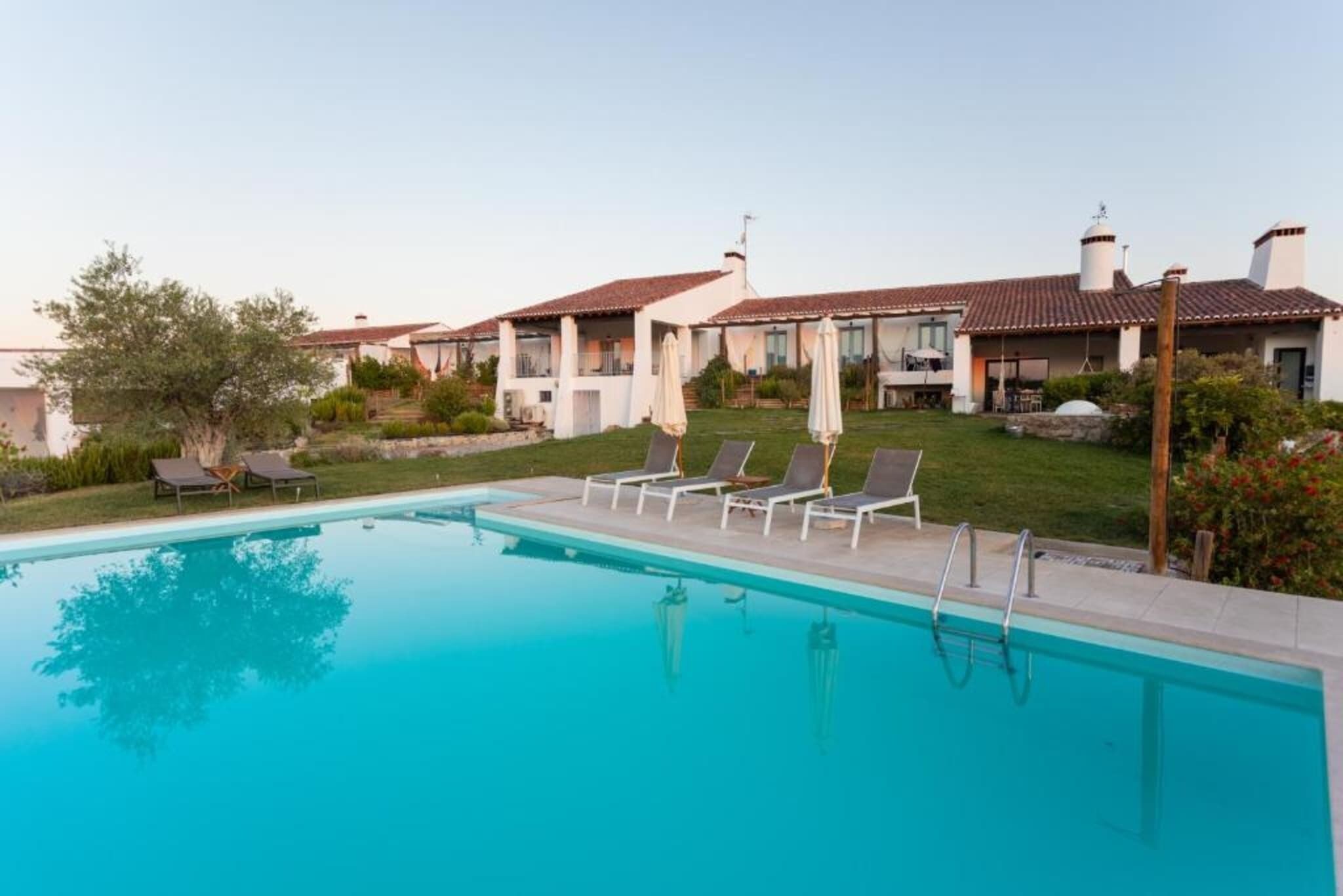 Ein Swimmingpool mit Liegestühlen, einem klaren Himmel und einer Reihe von Gebäuden mit roten Ziegeldächern.