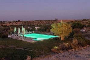 Piscina com espreguiçadeiras e guarda-sóis, cercada por um jardim paisagístico e vista para uma paisagem montanhosa.