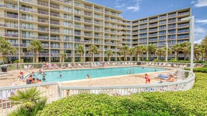 Un hôtel à plusieurs étages doté d’une piscine, entouré de palmiers et d’une clôture blanche.