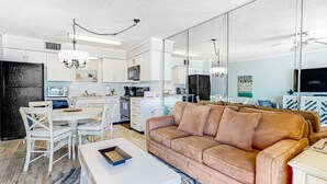 Une cuisine moderne avec des meubles blancs, une table à manger avec des chaises, un canapé marron et une table basse blanche.