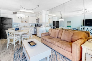 A modern kitchen with white cabinets, a dining table with chairs, a brown sofa, and a white coffee table. - Gulf-view condo with central AC, WiFi, laundry, pools, gym & tennis (Orange Beach)