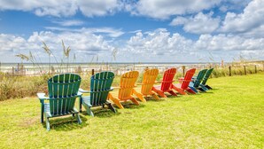 Une rangée de chaises Adirondack aux couleurs vives, disposées sur une pelouse, avec vue sur la plage et l’océan.