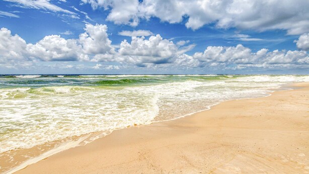 Une plage avec des vagues, un ciel dégagé et des nuages.
