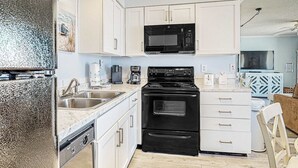 Une cuisine moderne avec des meubles blancs, un micro-ondes noir, une cuisinière et une machine à café.