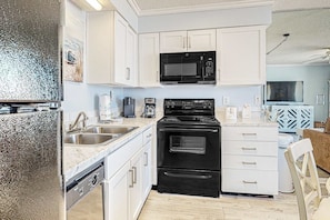 A modern kitchen with white cabinets, a black microwave, a stove, and a coffee maker. - Gulf-view condo with central AC, WiFi, laundry, pools, gym & tennis (Orange Beach)