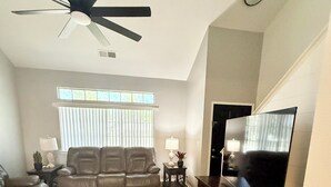 Una sala de estar con ventilador de techo, sofá de cuero, mueble para televisión y una alfombra grande.