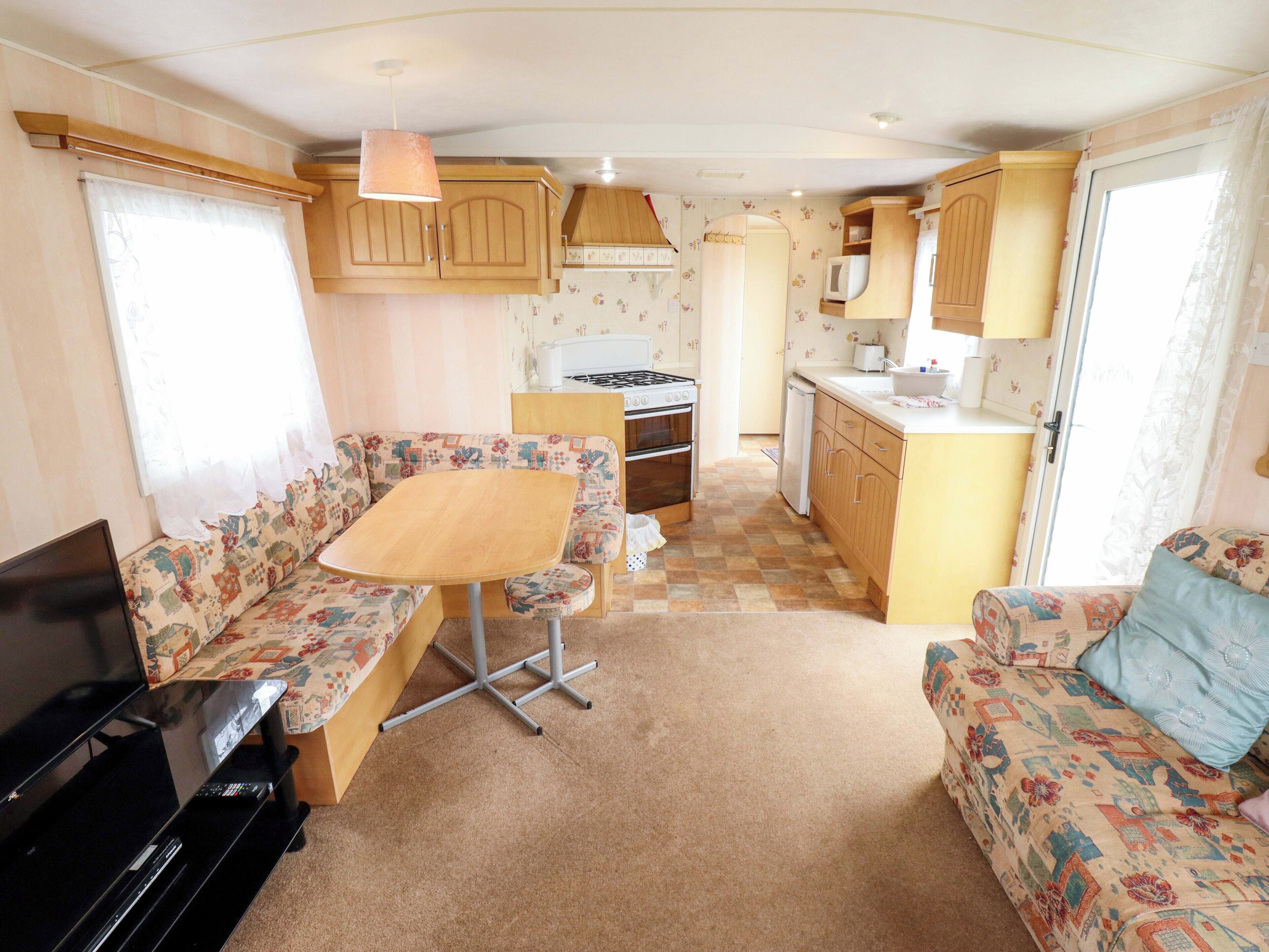 Interior compacto de una caravana con kitchenette, zona de comedor y espacio para sentarse.