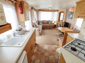 A compact RV kitchen with a sink, stove, and a dining area with a table and chairs. - Sealands Ingoldmells (Skegness)
