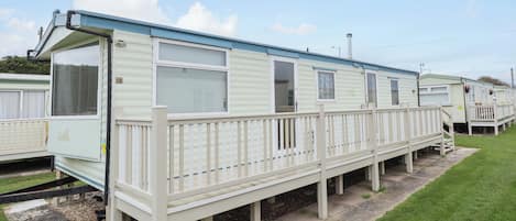 A row of mobile homes with a covered walkway and a grassy area in front.