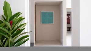 Een gang met een decoratief paneel, een potplant en een deur naar een andere kamer.