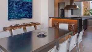 Een moderne eetruimte met een lange tafel, stoelen en een groot abstract schilderij.