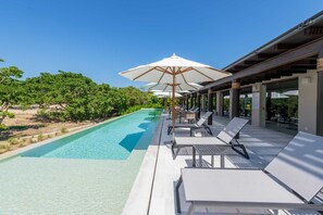 Ein Poolbereich mit Liegestühlen und Sonnenschirmen, umgeben von viel Grün.