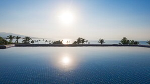 En klar, blå pool uden kant med udsigt til havet og palmer.