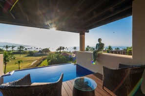 Ein Poolbereich mit Korbmöbeln, einer Statue und Blick aufs Meer.