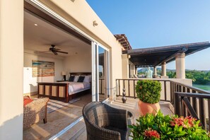 Ein Balkon mit einem Bett, Korbmöbeln, einem Deckenventilator und Blick auf die Landschaft.