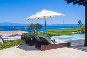 Ein Poolbereich mit Liegestühlen, einem großen Sonnenschirm und Blick auf den Ozean und den Golfplatz.