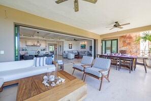 A spacious living area with a sofa, chairs, a coffee table, and a dining table. There is a kitchen in the background, and a balcony with a view. - Condo Zazil in Punta Mita (Punta de Mita)