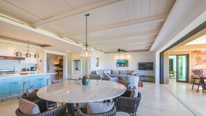 A spacious living area with a round dining table, comfortable seating, a kitchen with blue cabinets, and a large window. - Condo Zazil in Punta Mita (Punta de Mita)
