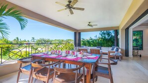 An outdoor dining area with a table set for four, wooden chairs, ceiling fans, and a view of greenery. - Condo Zazil in Punta Mita (Punta de Mita)