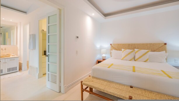A bedroom with a bed, bedside table, lamp, and a door leading to a bathroom. - Condo Zazil in Punta Mita (Punta de Mita)