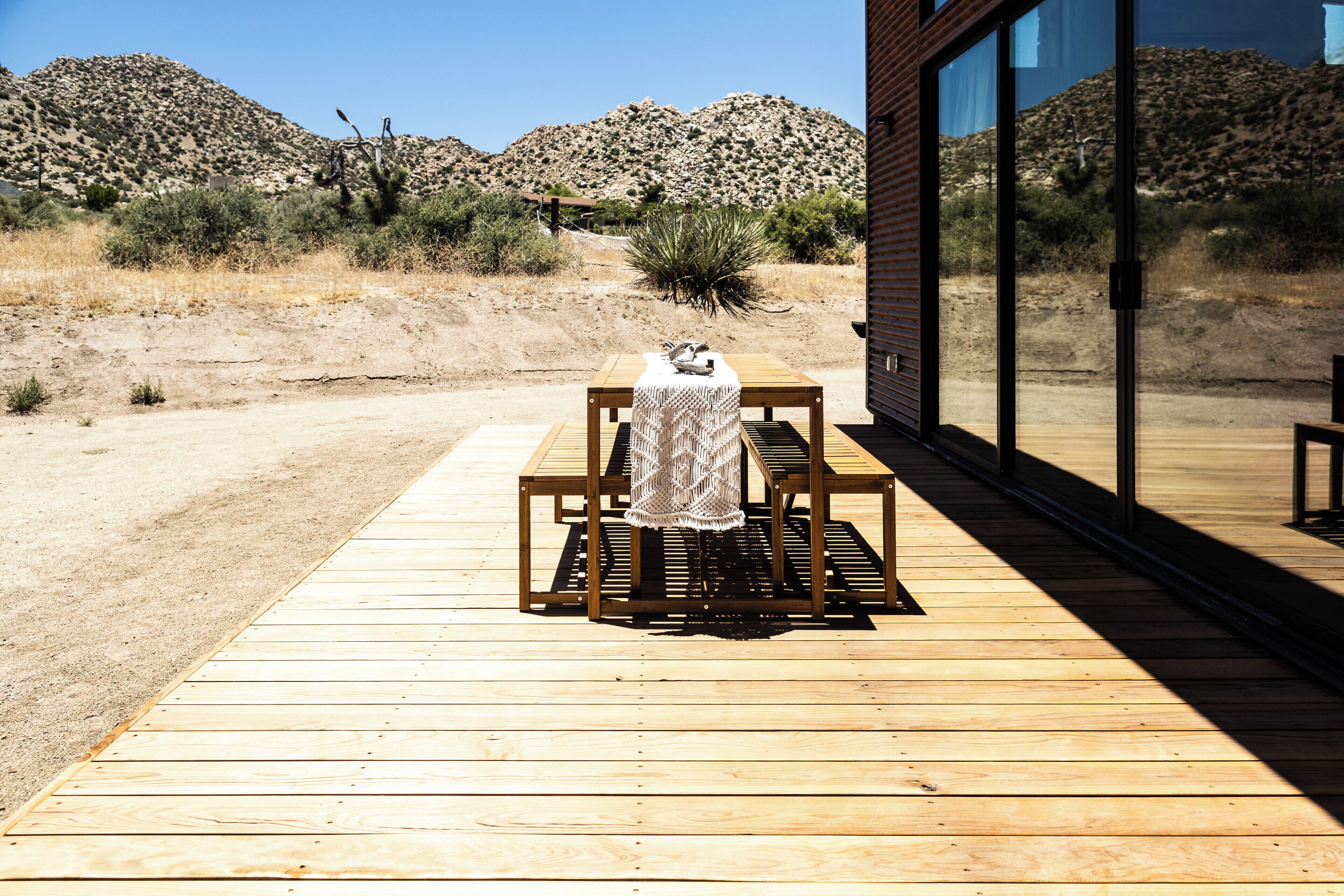 A wooden deck with a table and bench, a cactus, and a desert landscape in the background.