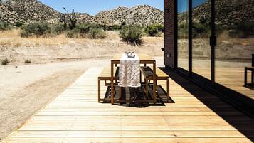 A wooden deck with a table and bench, a cactus, and a desert landscape in the background.