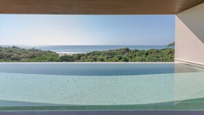Krystalklart udsyn til en pool med træloft, omgivet af grønt og med udsigt over en strand.