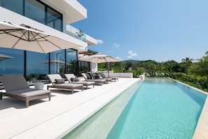 A modern poolside area with lounge chairs and umbrellas, a clear pool, and a view of greenery and hills. - Casa Todos Juntos in Punta Mita (Punta de Mita)