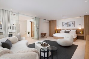 A modern hotel room with a large bed, a sitting area with a sofa and armchair, a small table, and a glass-enclosed shower area. - Casa Todos Juntos in Punta Mita (Punta de Mita)
