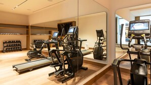 Une salle de sport équipée de tapis de course, de vélos elliptiques et d’un mur recouvert de miroirs.